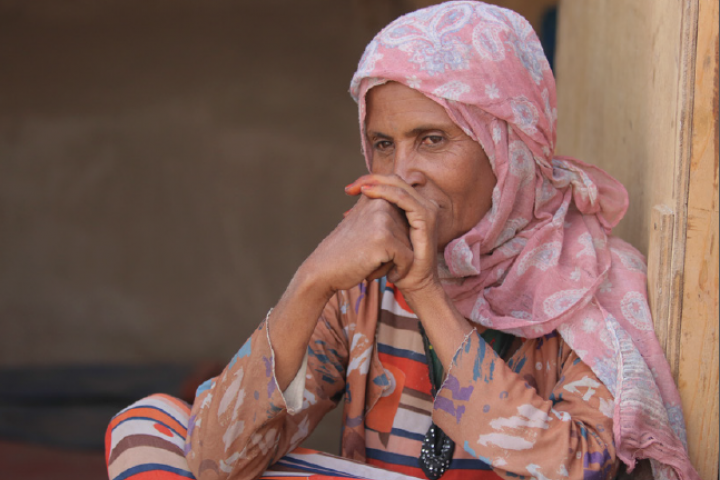 Old woman seated gazing away with hands crossed in front of her face