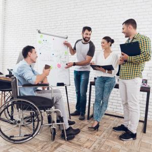 Photo showing a team of office employees including a man with disability using a wheelchair discussing work issues